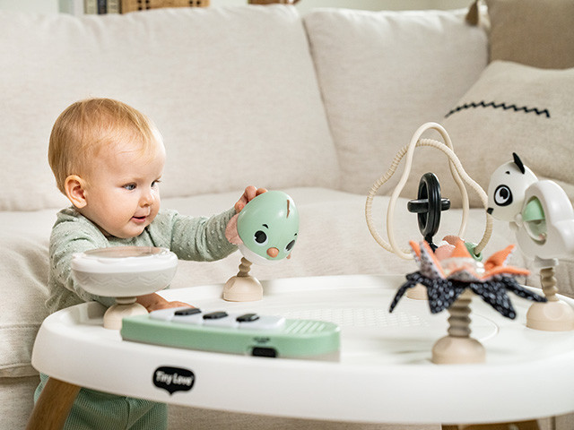 Criança a brincar com mesa de atividades redonda com várias peças coloridas