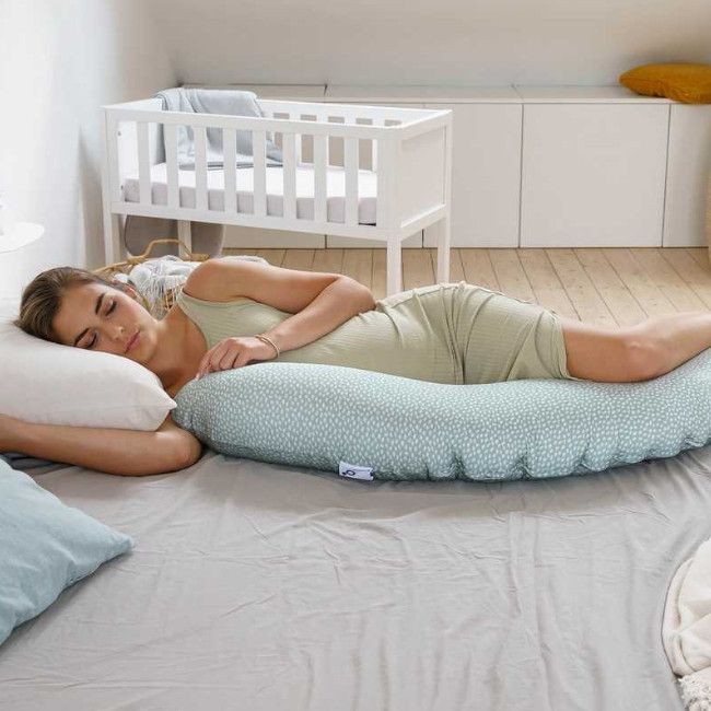 Mulher deitada na cama a abraçar almofada grande azul claro com bolinhas brancas