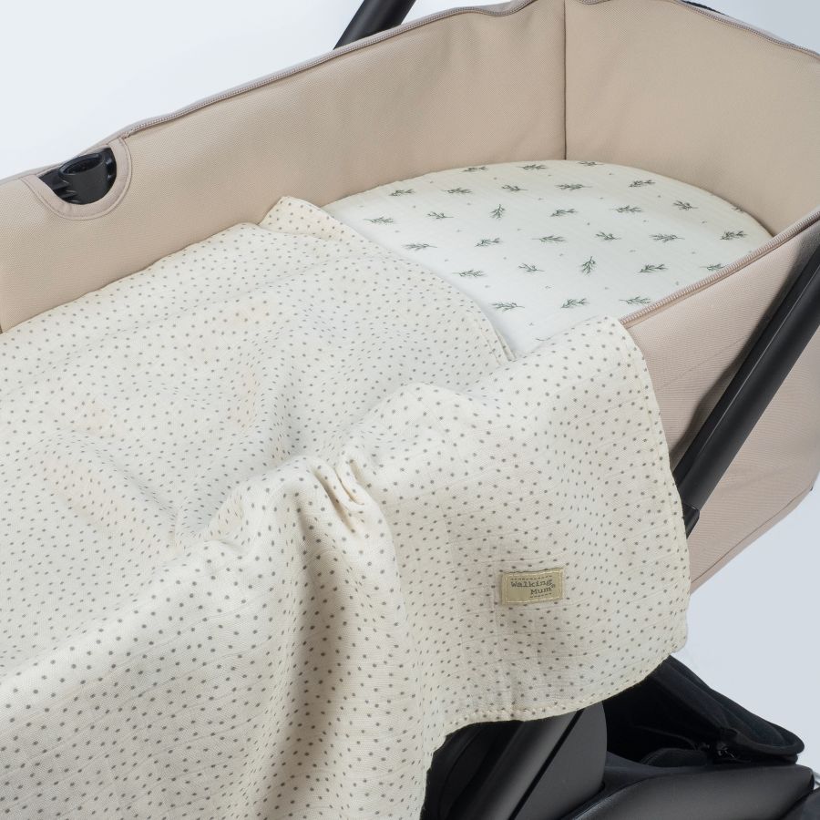 Cama/moisés de bebé bege com manta creme às bolinhas e padrão verde no interior, montado em carrinho preto