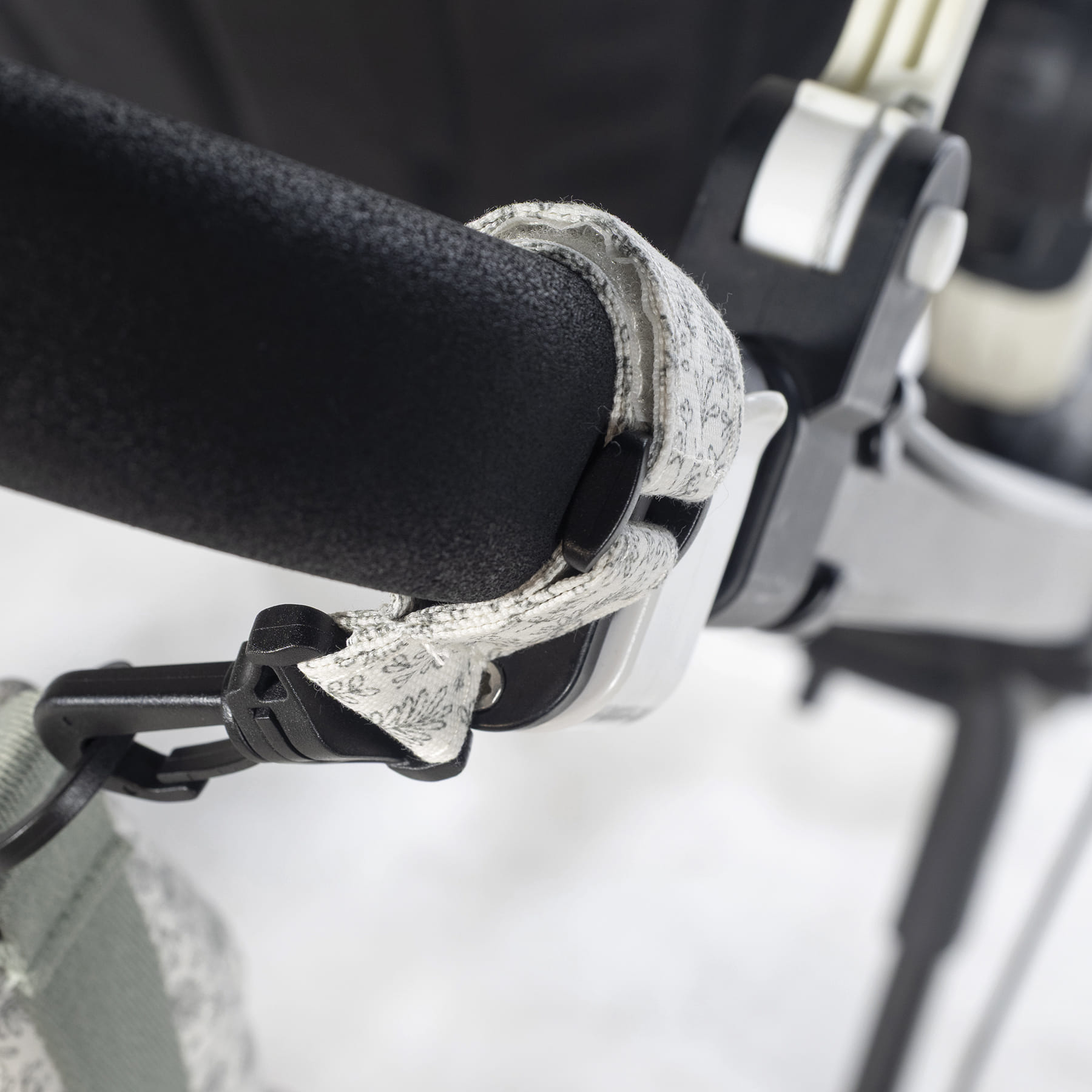 Alça almofadada preta e branca com padrão floral cinza fixa a estrutura metálica