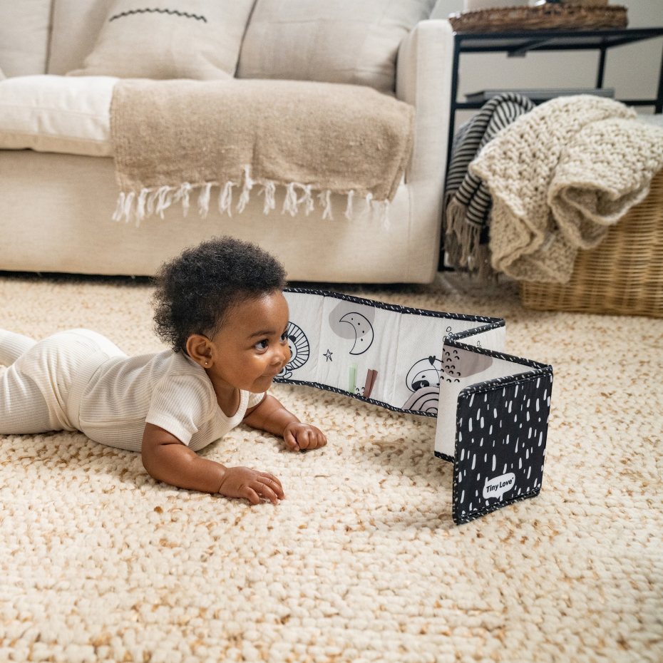 Bebé deitado em tapete a olhar para livro de pano com padrões em preto e branco