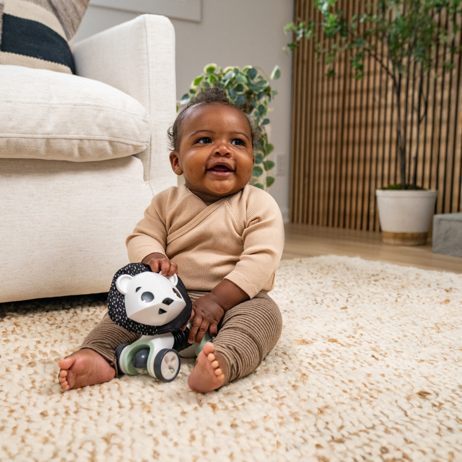 Bebé sentado a brincar com brinquedo de urso no tapete bege próximo a sofá e plantas