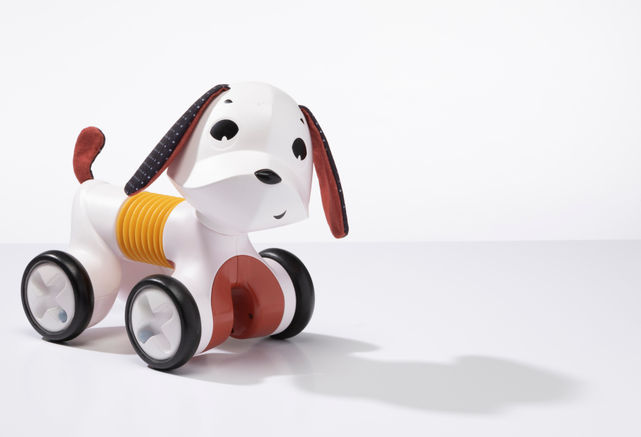 Brinquedo de cão branco com rodas preto e detalhes castanhos sobre superfície branca