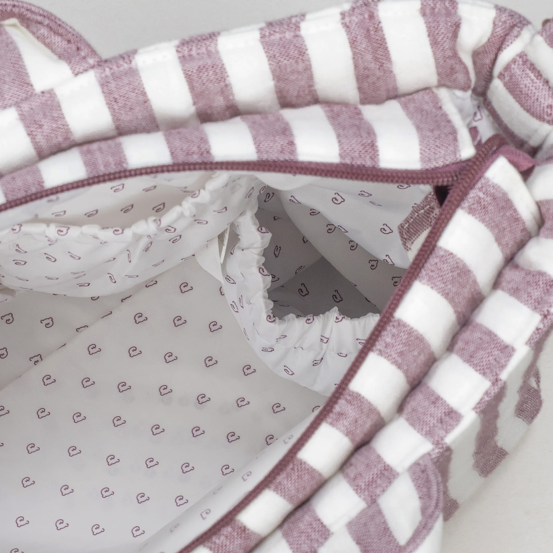 Interior de bolsa com padrão de riscas brancas e roxas e compartimentos elásticos internos