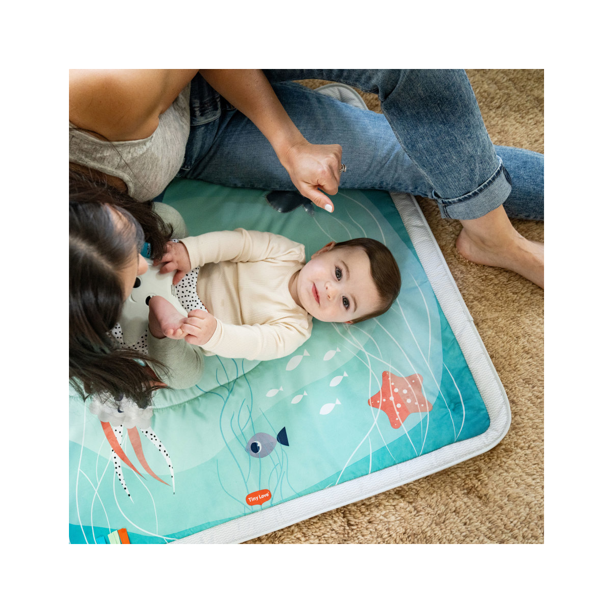 Bebé e mãe deitados num tapete macio azul com padrão subaquático