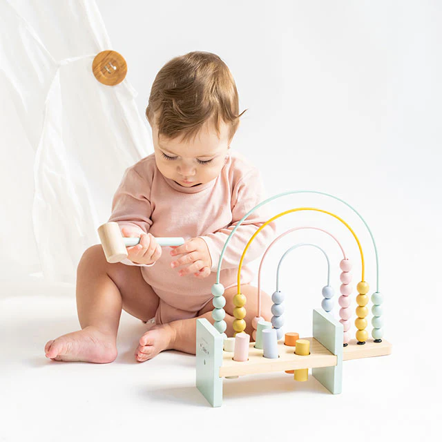 Bebé com body rosa brincando com brinquedo de contas coloridas em arcos metálicos.