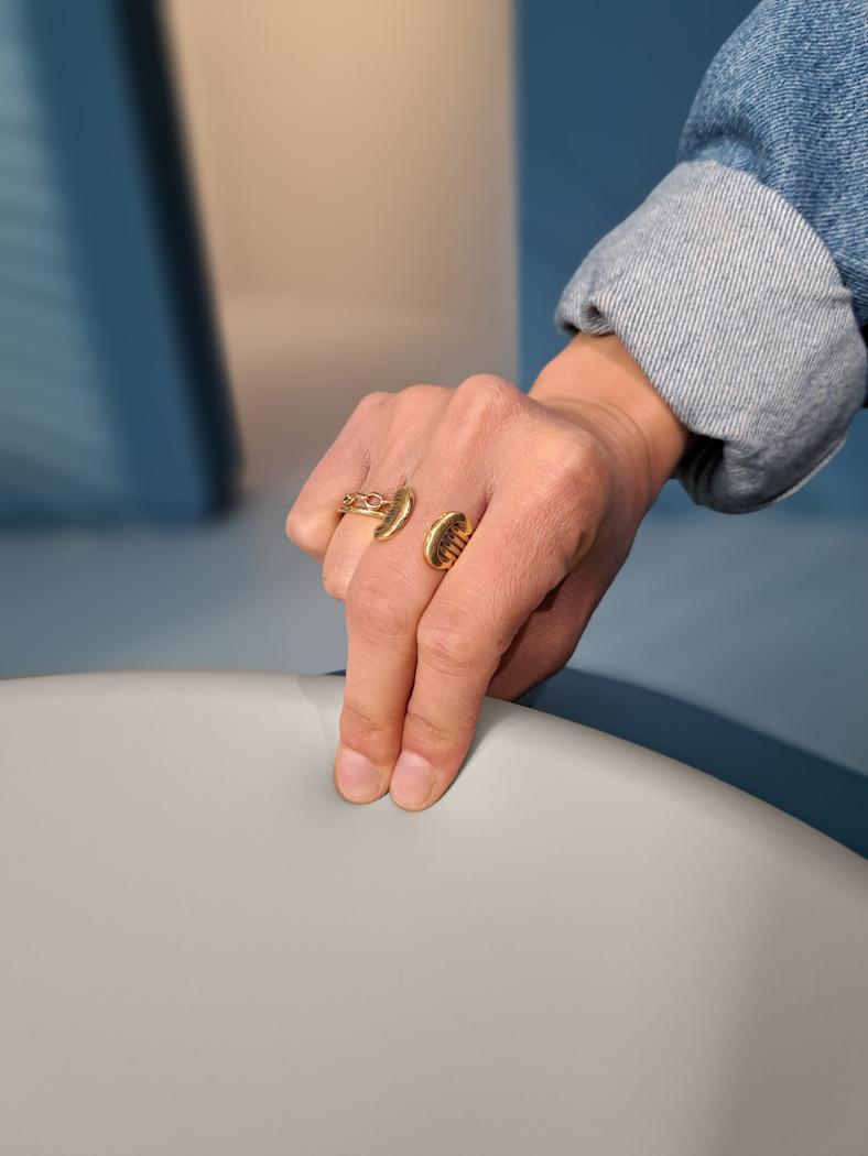 Mão com anel dourado aberto sobre superfície cinzenta