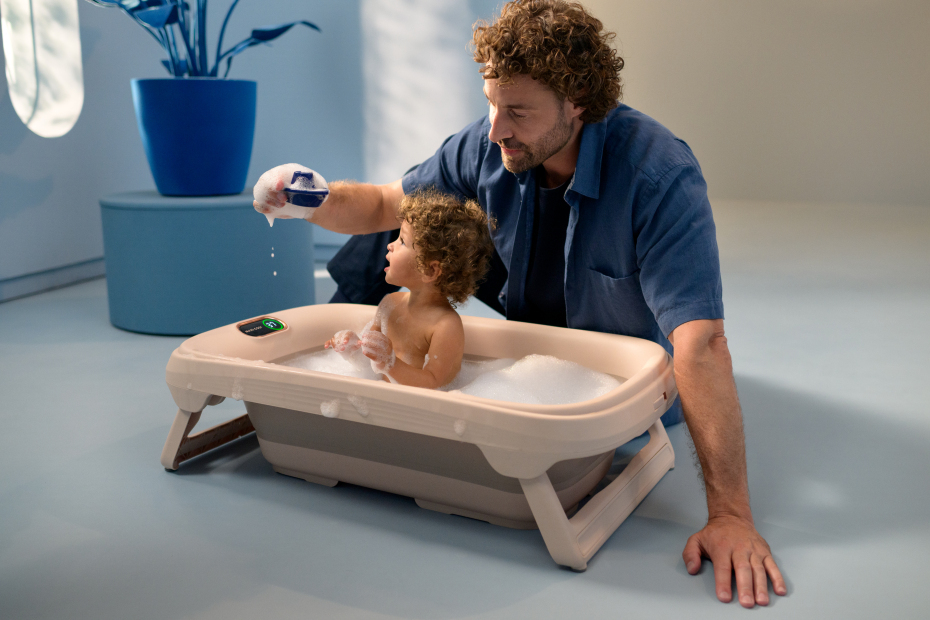 Banheira dobrável bege e cinza com espuma e criança a ser cuidada por homem