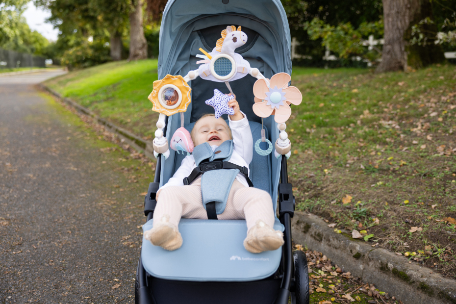 Bebé num carrinho azul com brinquedos pendurados em parque
