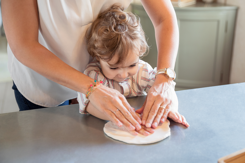 Adulto e criança a amassar massa branca numa bancada.