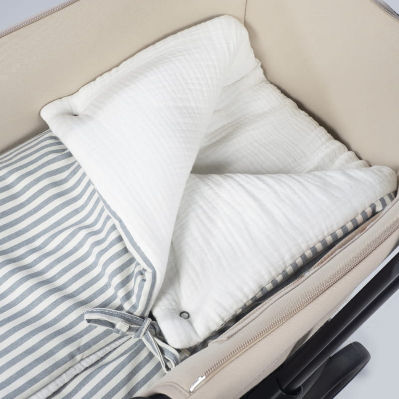 Cama de bebé bege com manta branca e cobertor riscado azul e branco