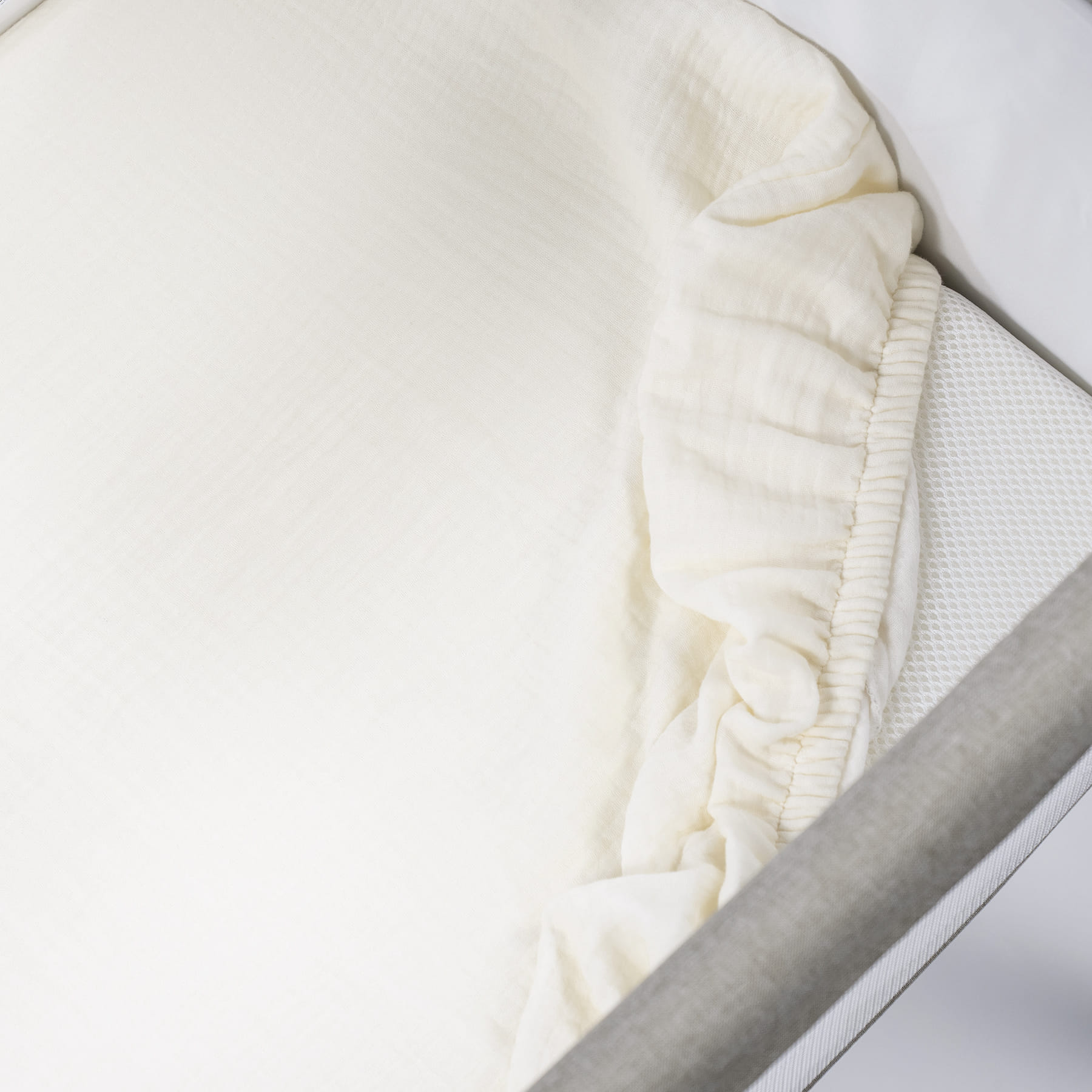 Lençol branco de algodão com elástico numa superfície branca com moldura cinza.