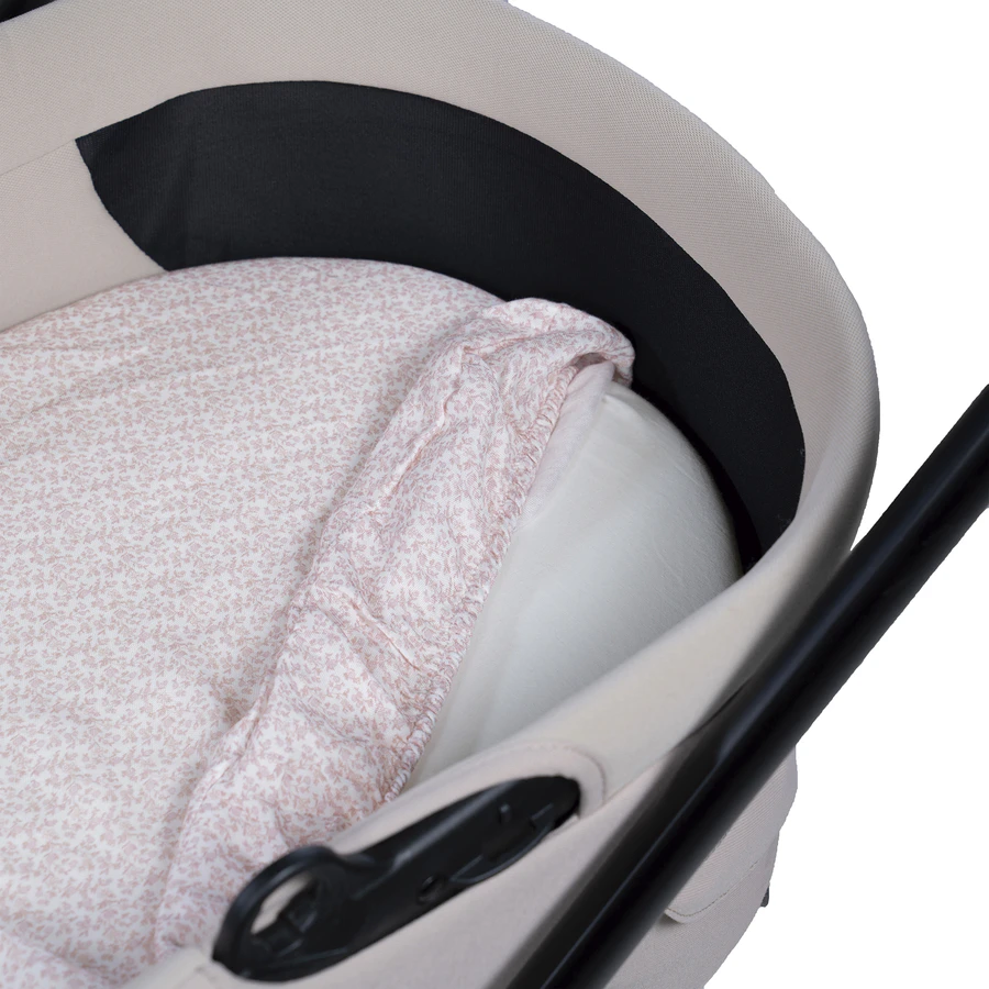 Berço portátil bege com almofada branca e lençol rosa claro com padrão floral