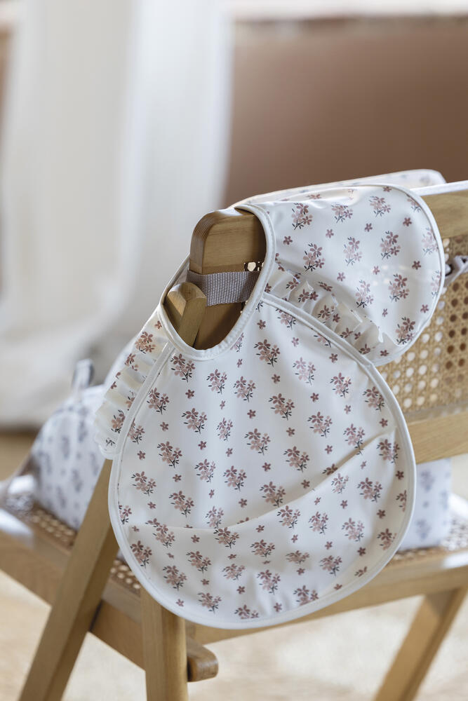 Babete para bebé com padrão floral pendurado numa cadeira de madeira com encosto de palhinha