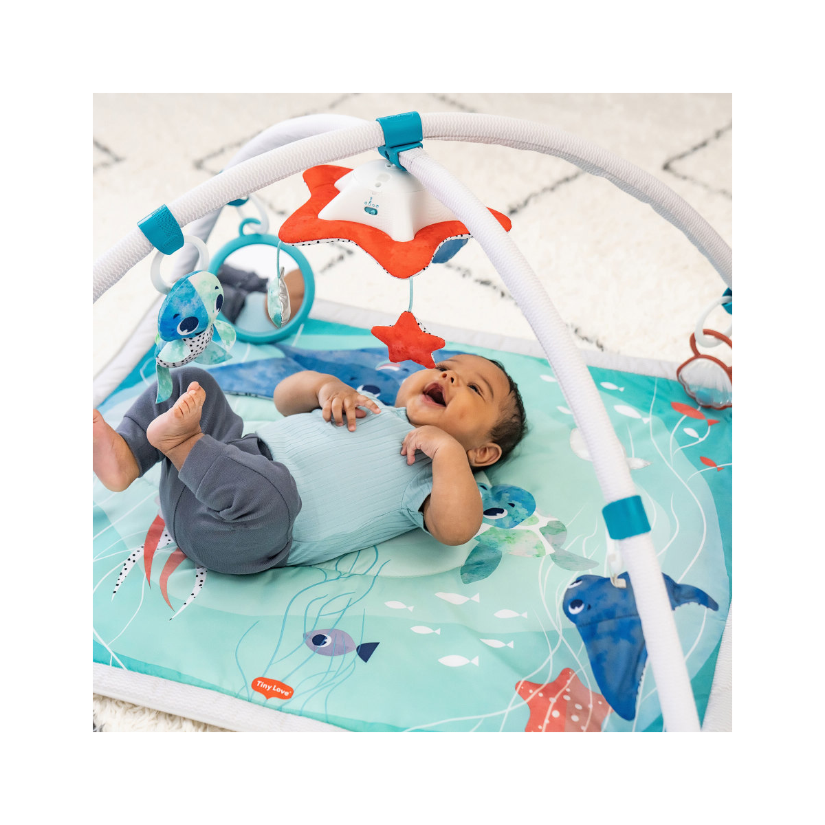 Tapete de atividades azul com brinquedos pendentes e bebé a brincar