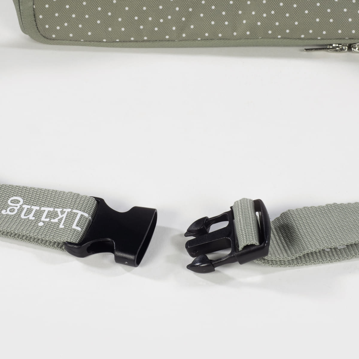 Fivela de mochila preta com correia verde cinzento e padrão de bolinhas brancas