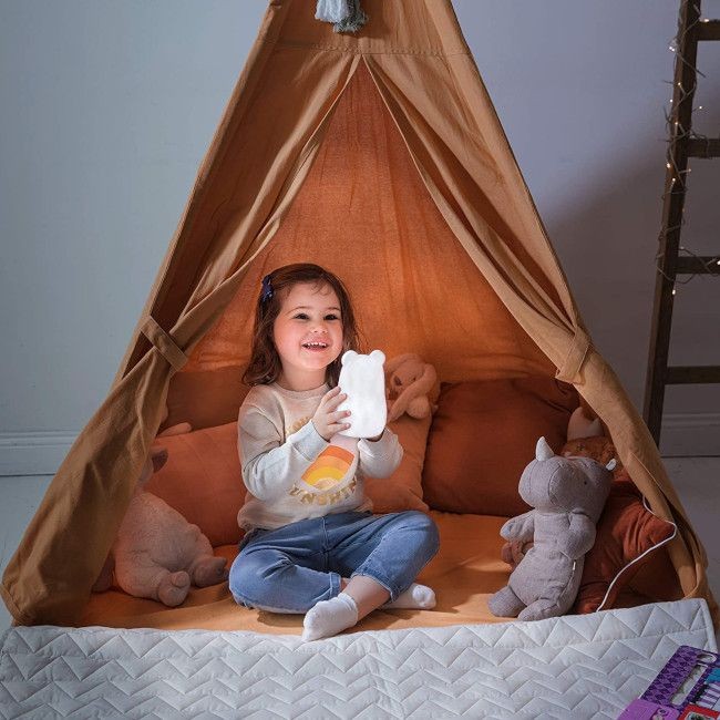 Criança sentada em tenda de tecido com almofadas e peluches
