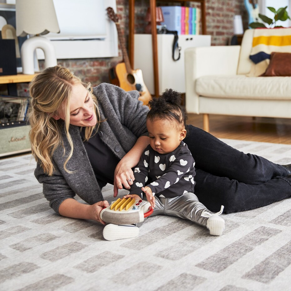 Mulher e criança sentadas no chão com brinquedo de madeira sobre tapete cinza
