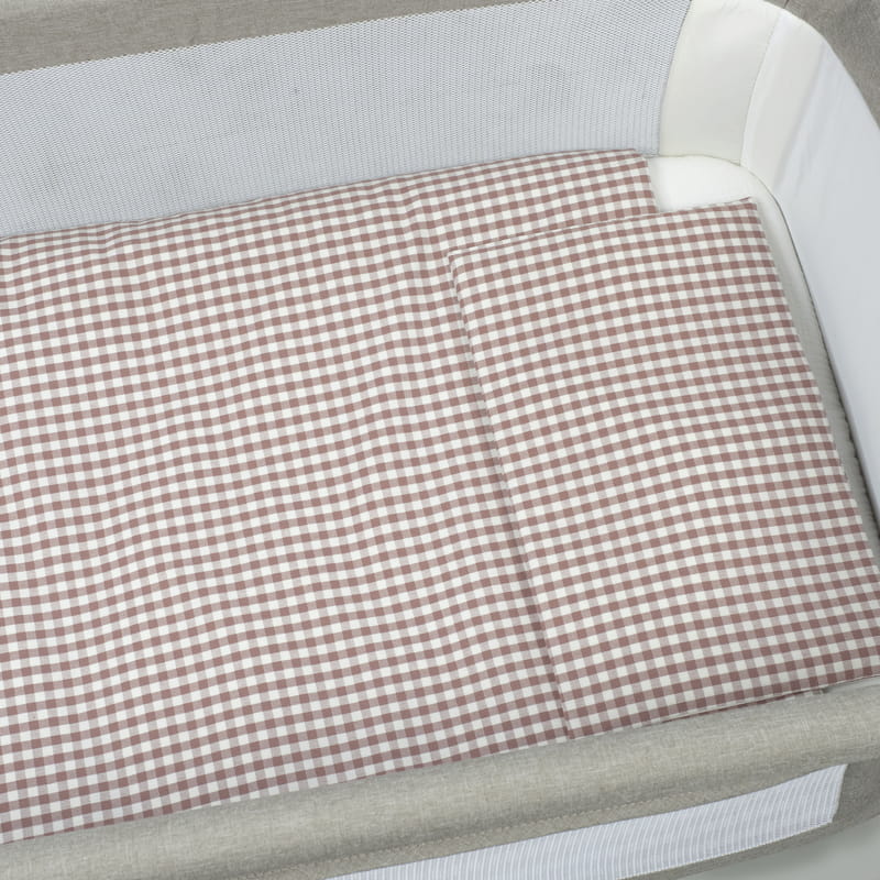 Colchão e almofada xadrez branco e castanho numa cama de bebé com laterais de rede