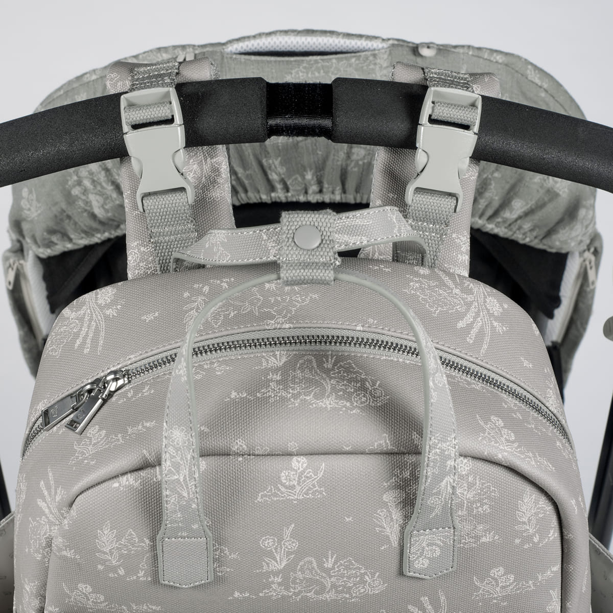 Mochila cinza com padrão floral branco fixada a barra acolchoada preta de carrinho de bebé