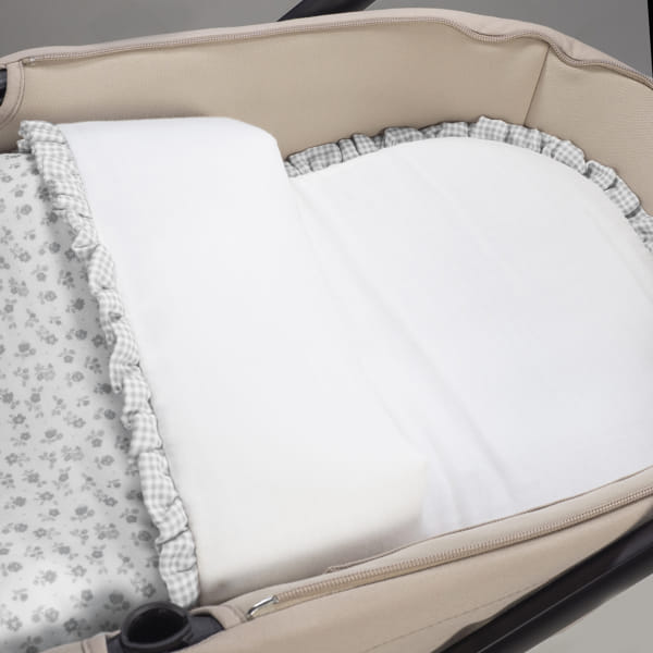 Berço portátil bege com edredão branco e lençol com padrão de flores cinza
