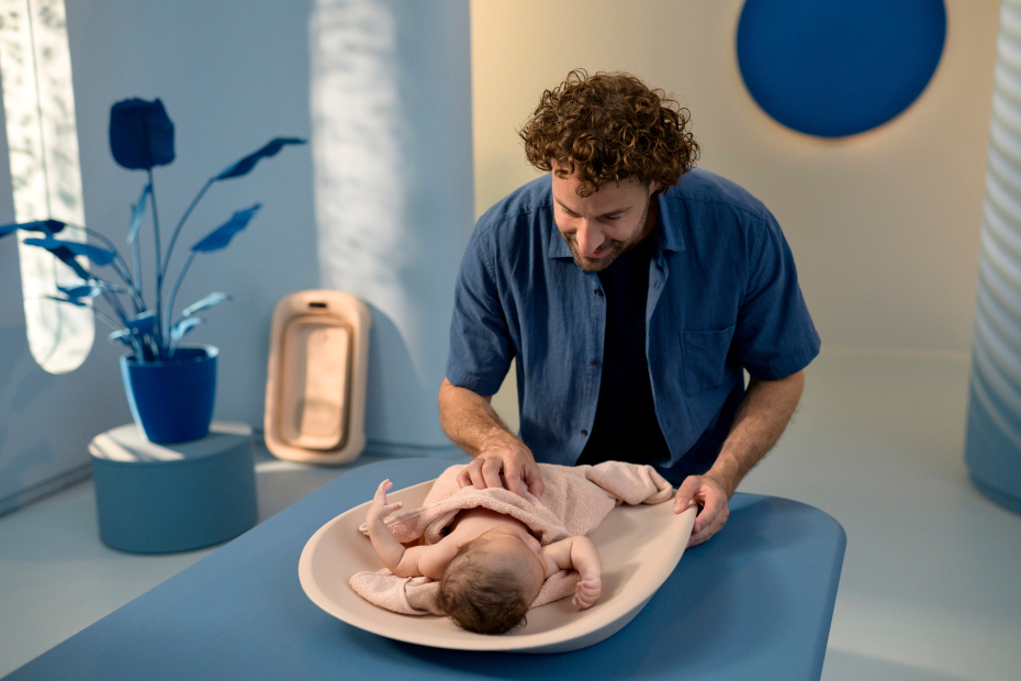 Bebé deitado numa cama com homem a cuidar em ambiente azul