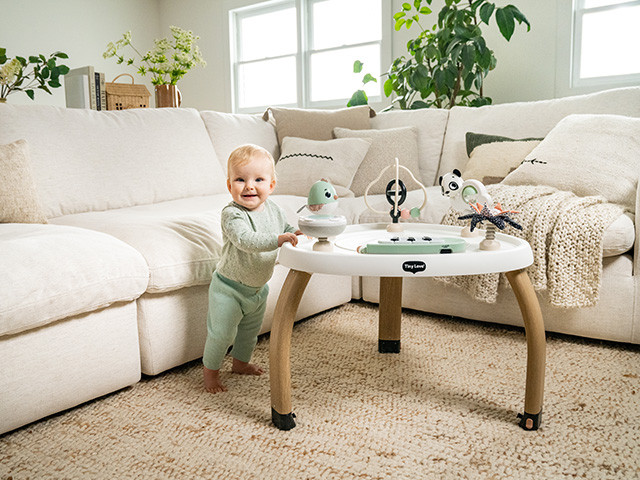 Criança com mesa de atividades branca e pernas de madeira em sala de estar acolhedora