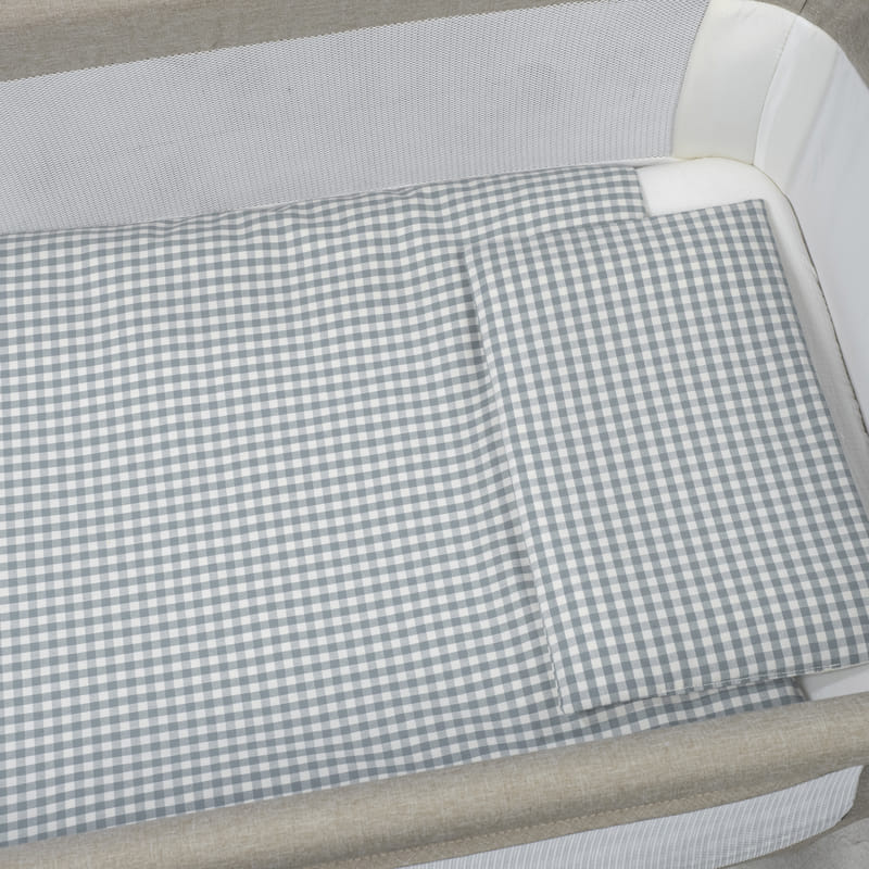 Colchão e almofada xadrez cinza branco em cama de bebé com laterais em rede