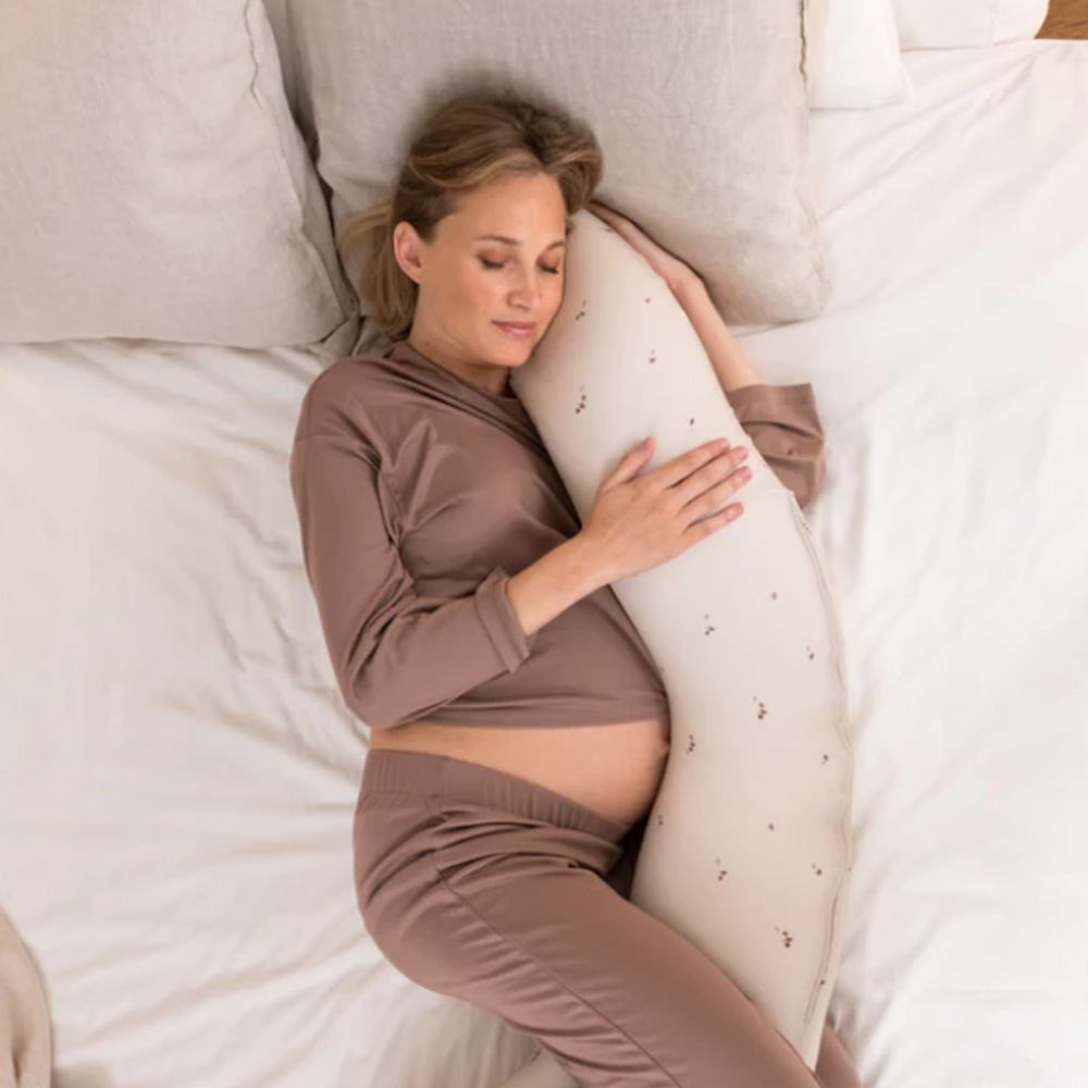 Mulher grávida deitada abraçando travesseiro de corpo creme com flores pequenas