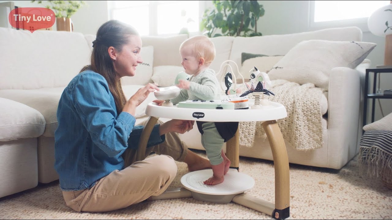 Cadeira de bebé branca com estrutura bege claro da marca Tiny Love com mulher e bebé num ambiente doméstico