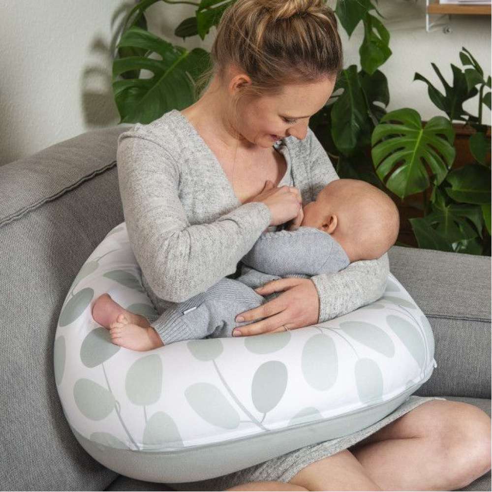 Mulher amamentando bebé com travesseiro estampado de folhas cinza e branco sentado no sofá
