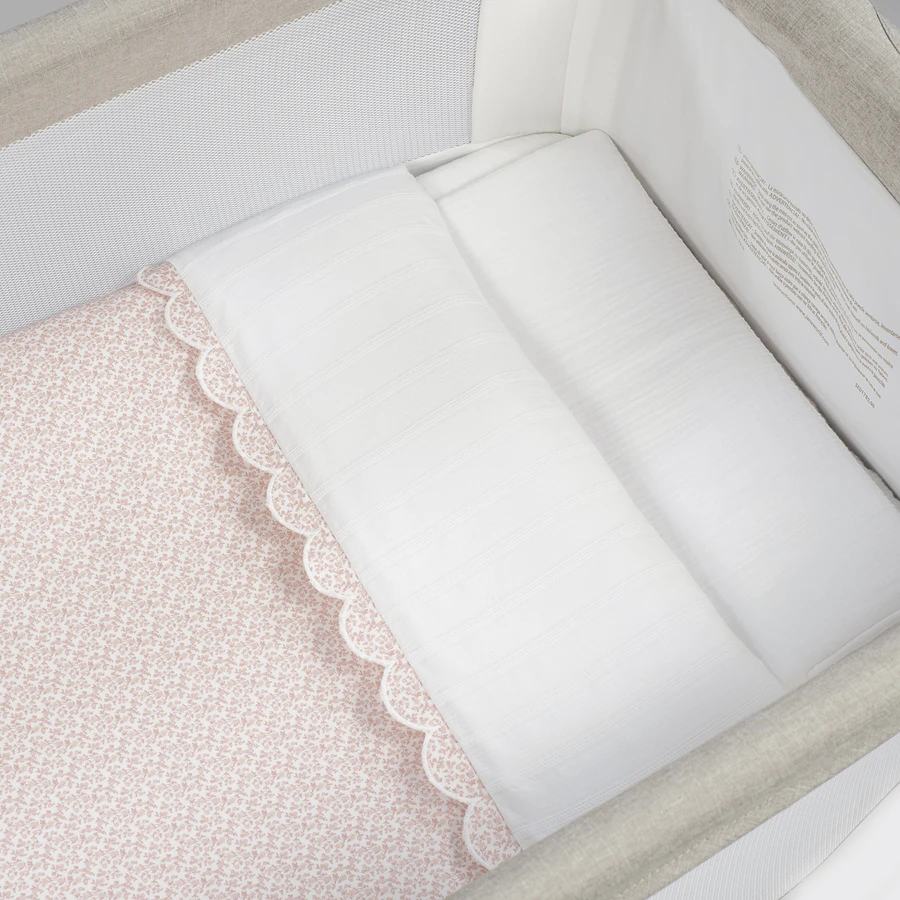 Berço branco com roupa de cama rosa claro com padrão floral e cobertor branco com borda festonada