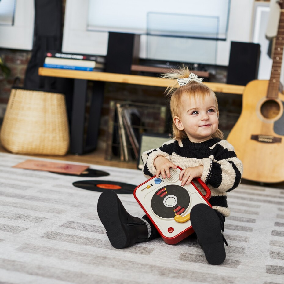 Criança a brincar com brinquedo gira-discos em sala com guitarra e cesto ao fundo