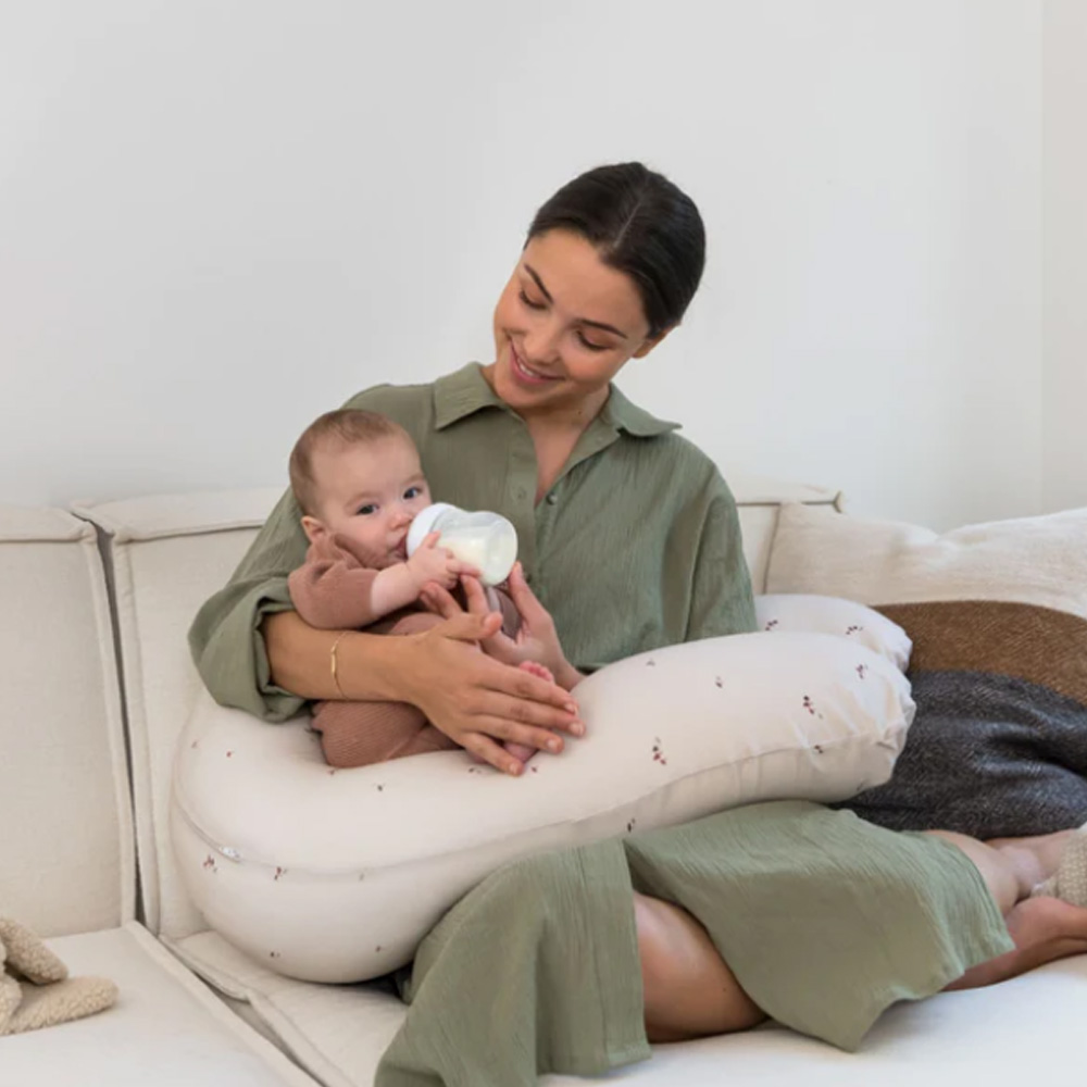 Mulher a amamentar bebé com almofada de amamentação numa sala clara