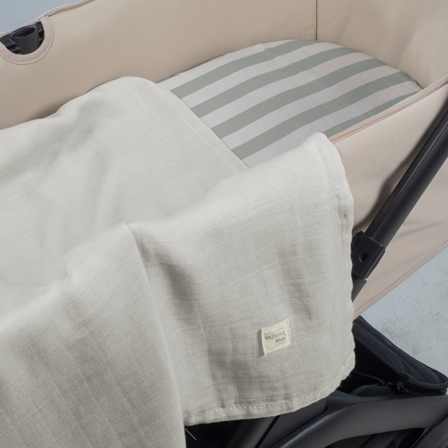 Cobertor branco em carrinho de bebé com almofada riscada cinza e branca