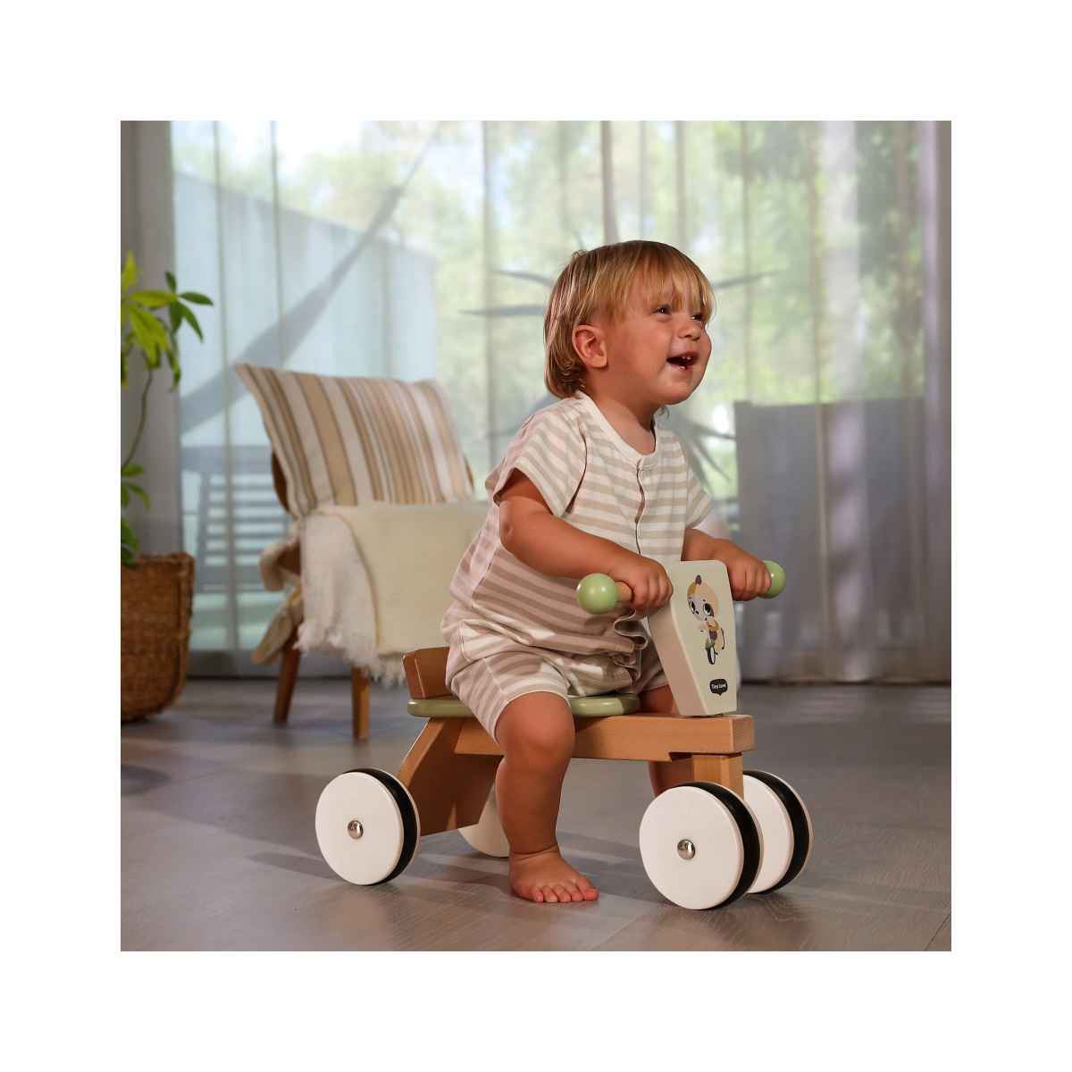 Criança num triciclo de madeira com rodas brancas e pretas em casa