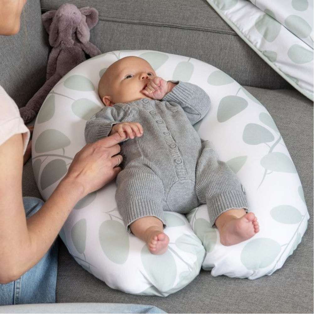 Almofada de amamentação branca com padrão verde, bebé de macacão cinzento, mão adulta e peluche elefante