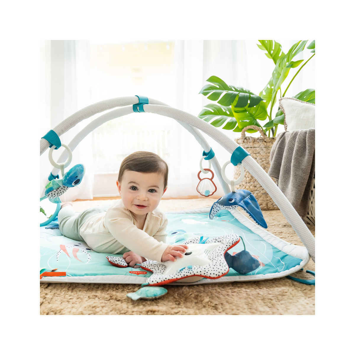 Bebé a brincar num tapete de atividades azul claro com brinquedos marinhos pendurados