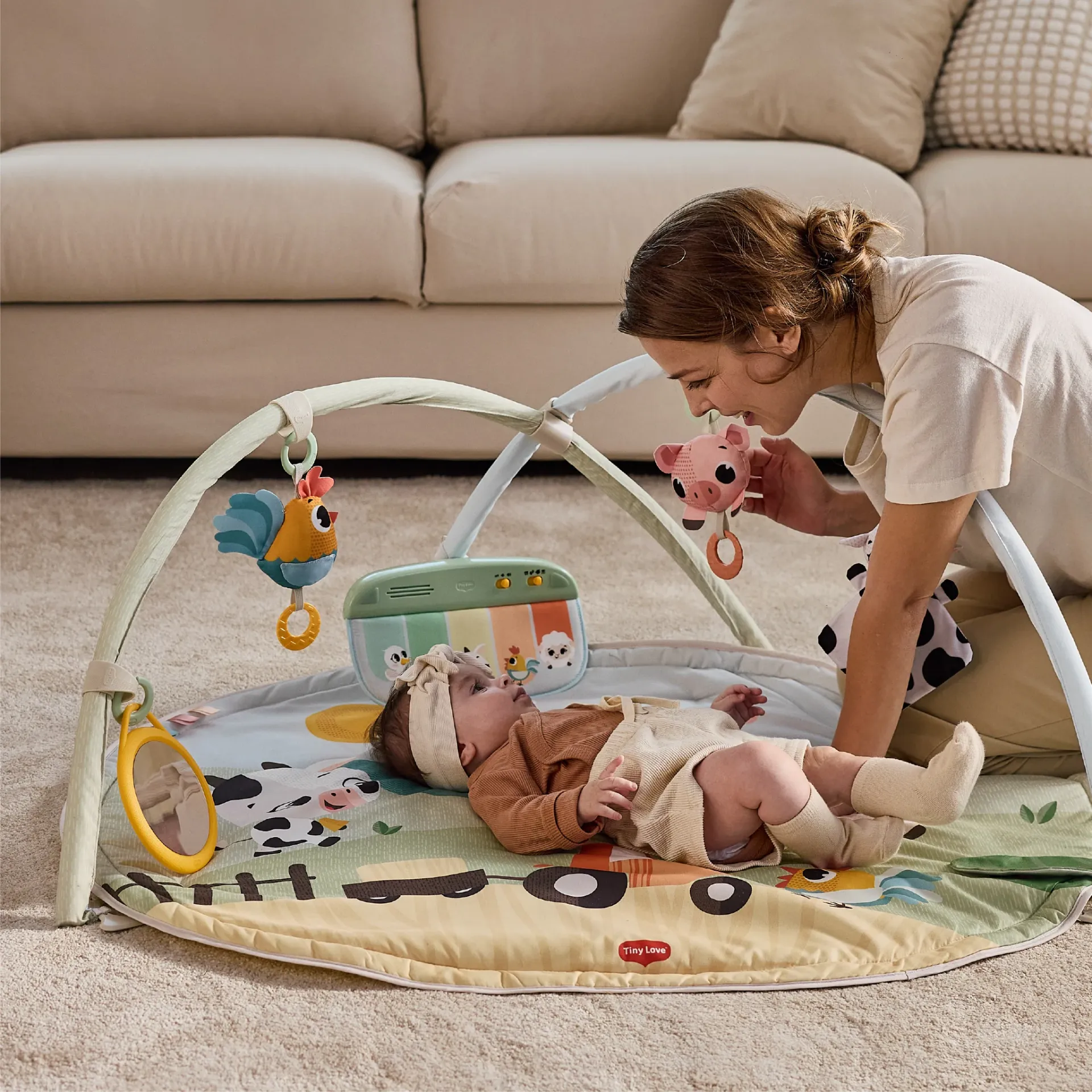 Tapete para bebé com arco de atividades e peluches pendurados em ambiente interior com mulher e bebé.