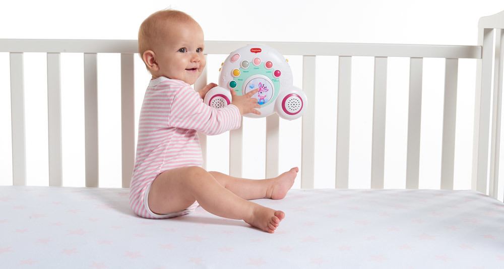 Bebé sentado em berço branco com brinquedo musical colorido