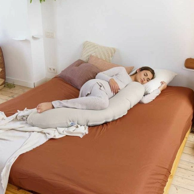 Mulher deitada numa cama com travesseiro de corpo longo bege e lençol castanho