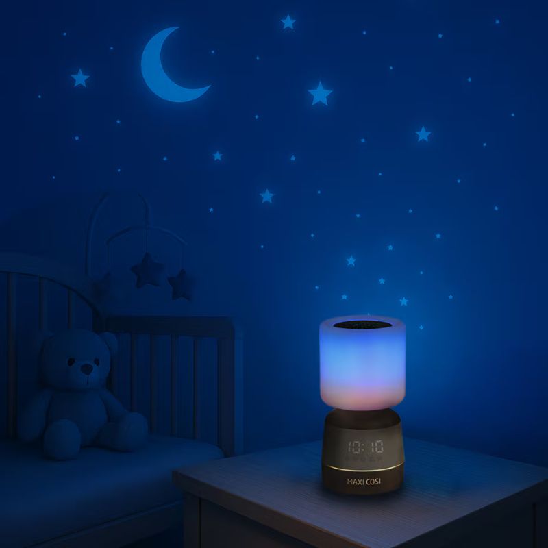 Lâmpada de mesa com luz azul e rosa, relógio digital e texto MAXI COSI, berço e decoração de estrelas e lua na parede