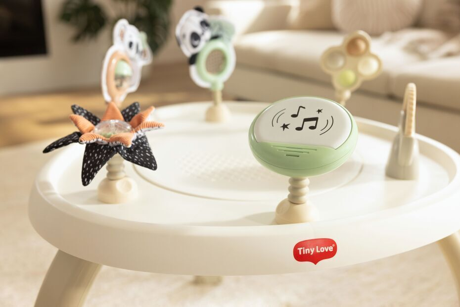 Mesa de atividades infantil branca com brinquedos montados e logótipo Tiny Love