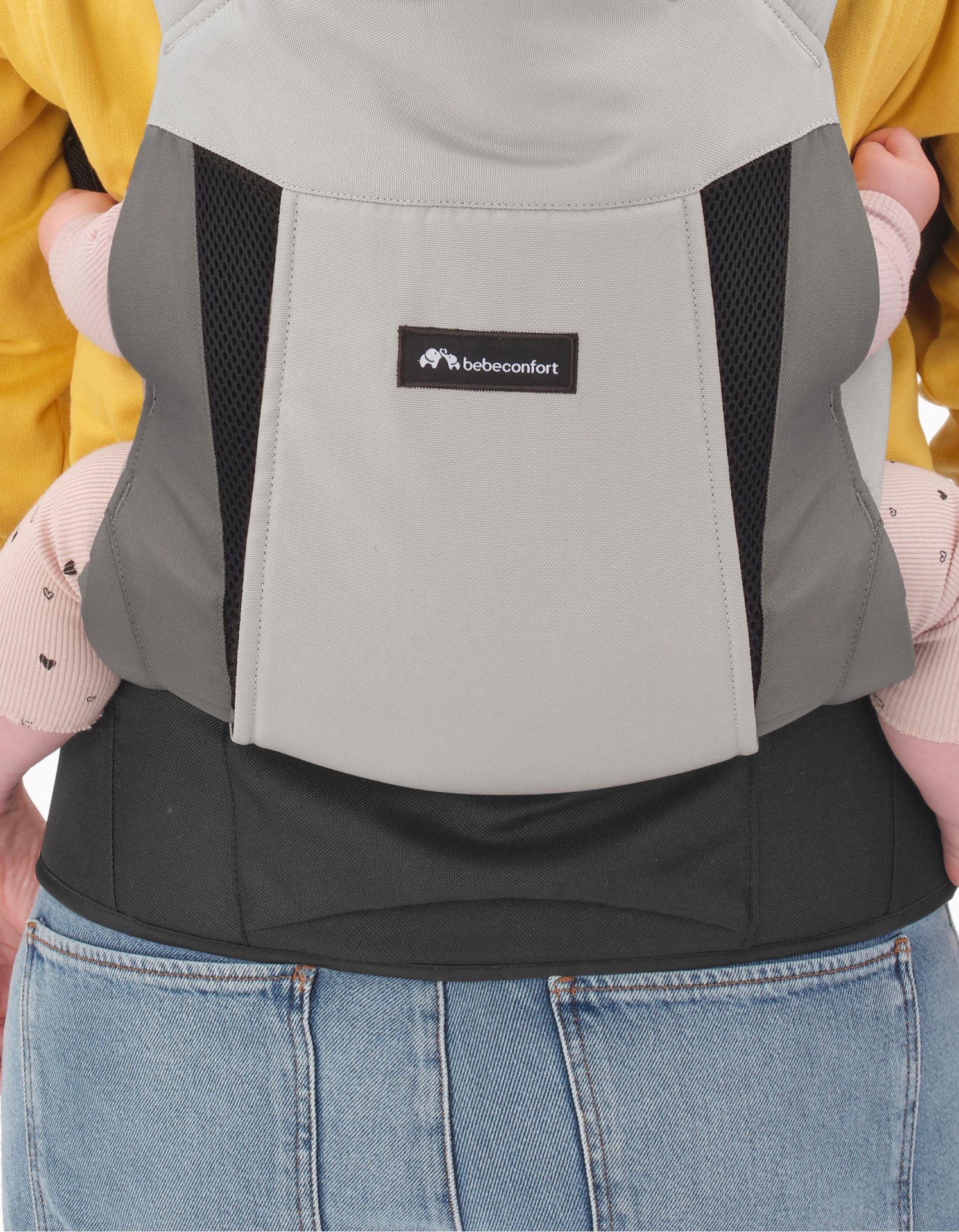 Porta-bebés cinzento com etiqueta bebéconfort, usado com calças de ganga.