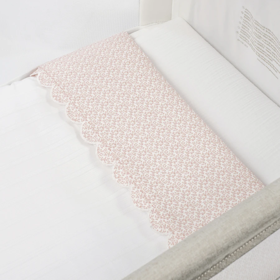Lençol branco e rosa estampado floral dentro de berço branco acolchoado