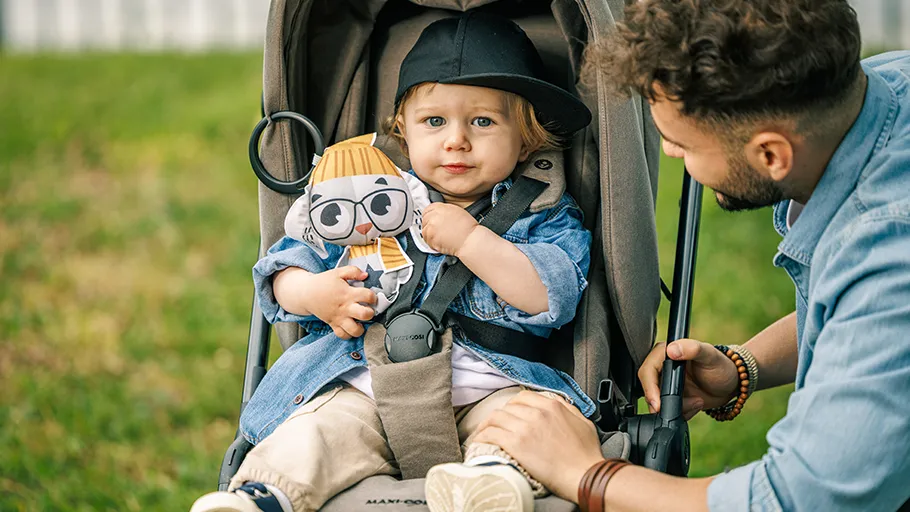 Bebé com peluche num carrinho cinzento com homem ao lado em relvado verde