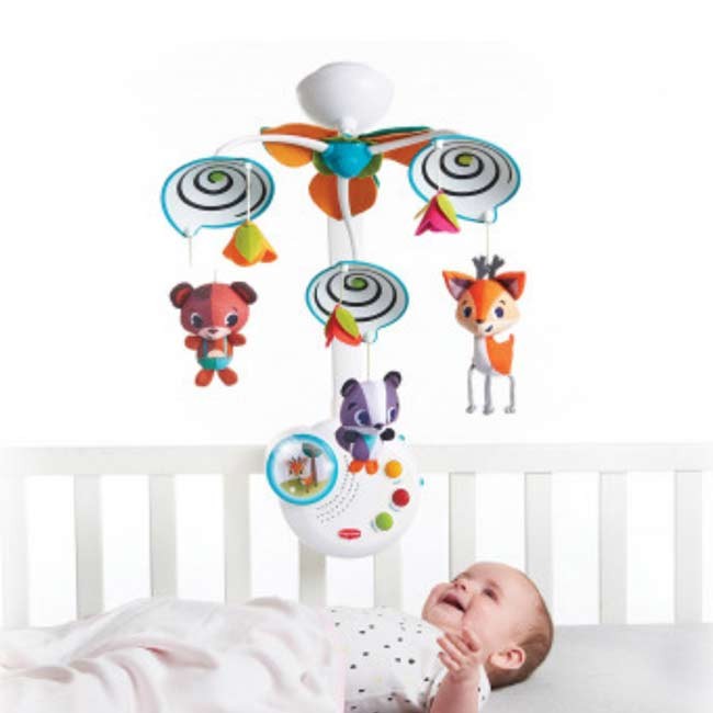 Móbile de berço com ursinho, raposa e texugo pendurados acima de bebé num berço branco