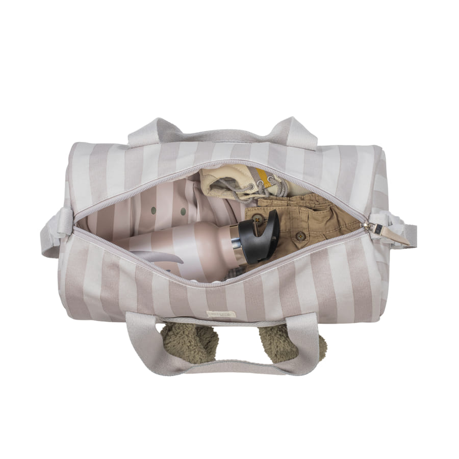 Mala de viagem pequena bege com riscas abertas, vista de cima com roupa, garrafa e brinquedo