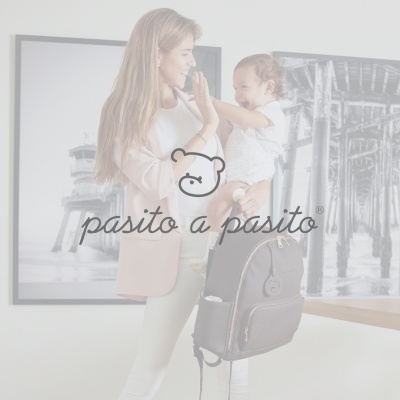 mochila preta com bolsos e fechos metálicos suspensa numa sala com mãe e criança ao fundo