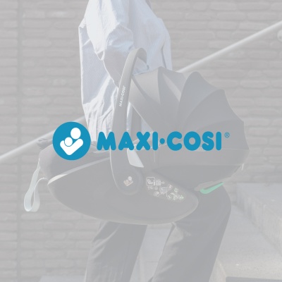 Cadeira auto bebé Maxi-Cosi preta com pega e etiquetas, parede de tijolos ao fundo